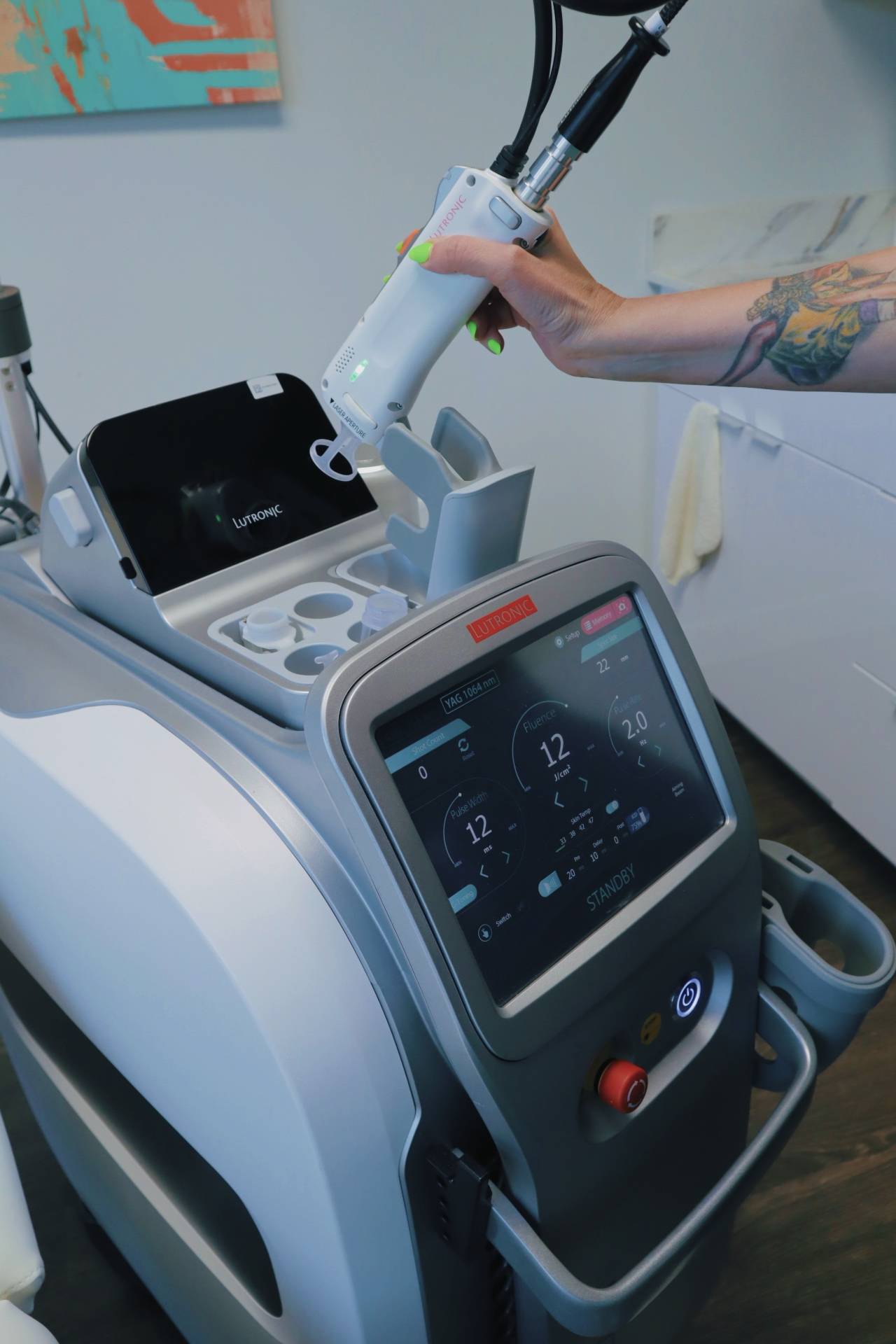 A technician lifting the Clarity II handpiece from its holder; the laser's screen reads YAG 1064 nm