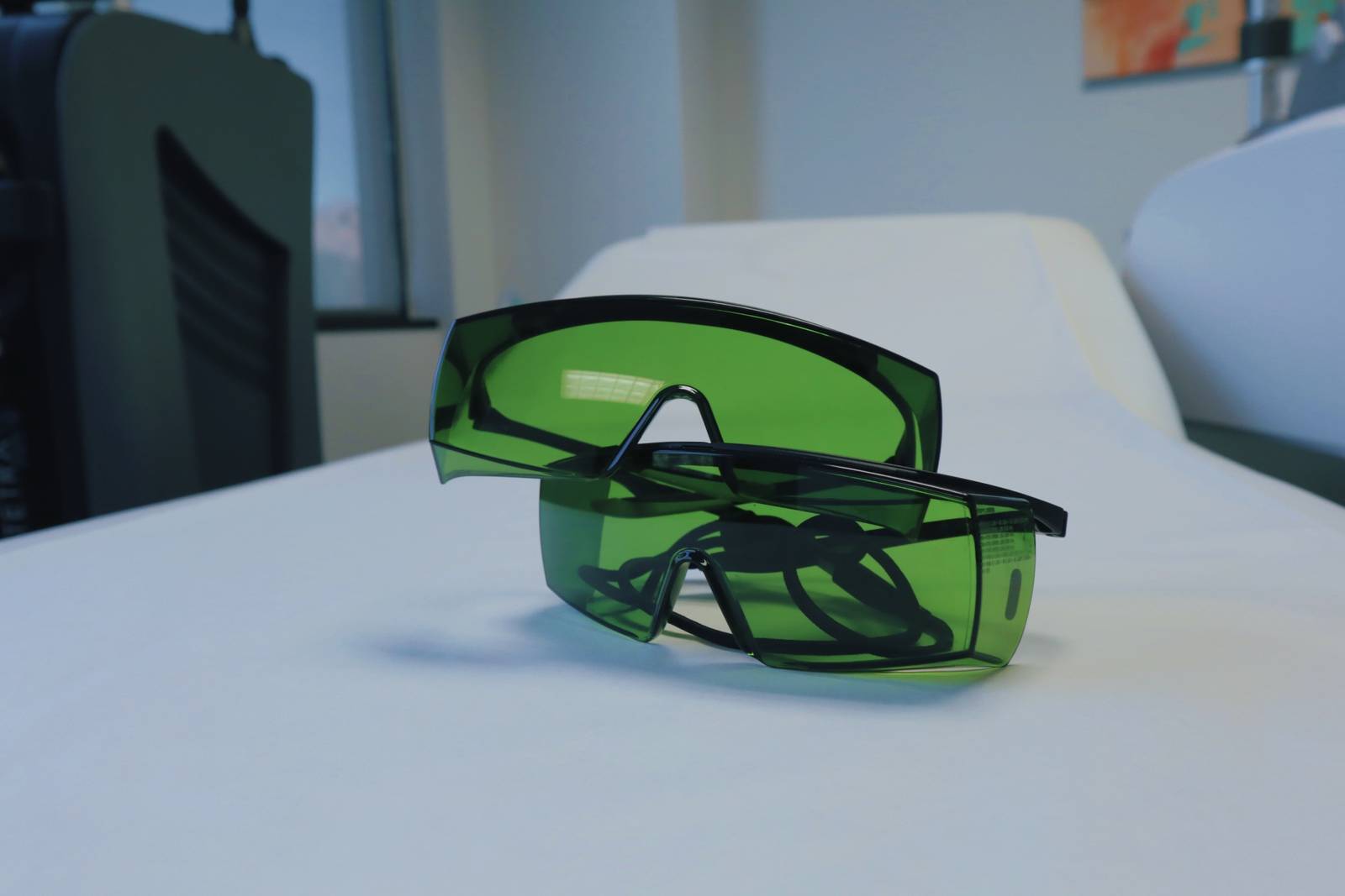 Two pairs of green-tinted laser safety glasses on a treatment bed
