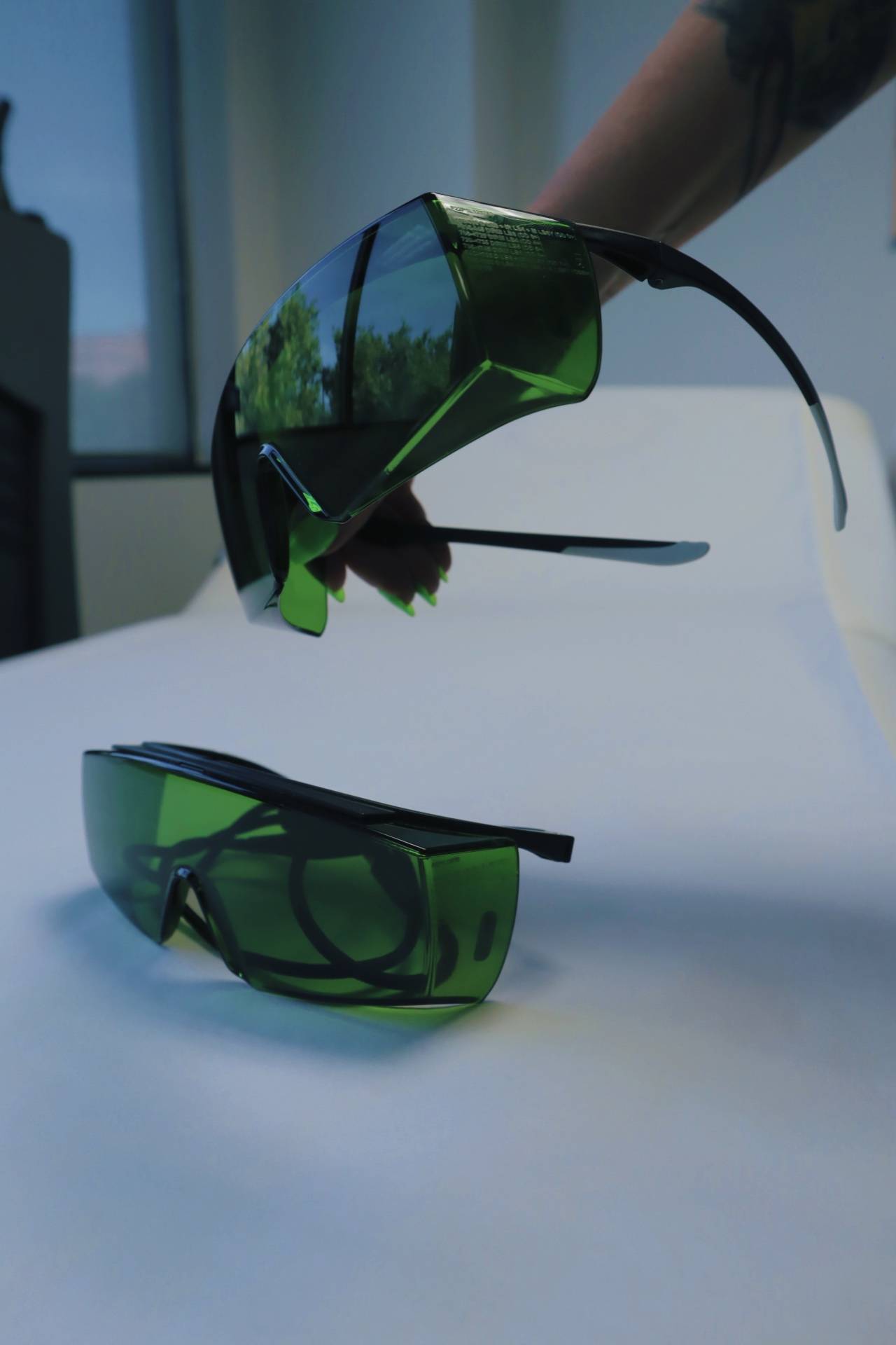 Laser safety glasses, one pair held up and another lying on the treatment bed
