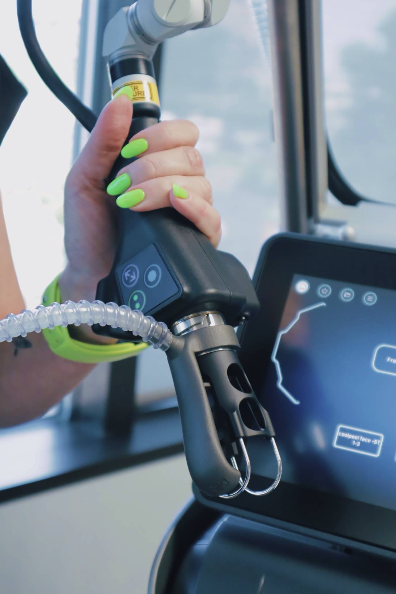 A hand holding the Tetra Pro CO2 laser handpiece beside the laser's screen